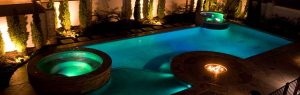 swimming pool with attached Jacuzzi and fire pit at night